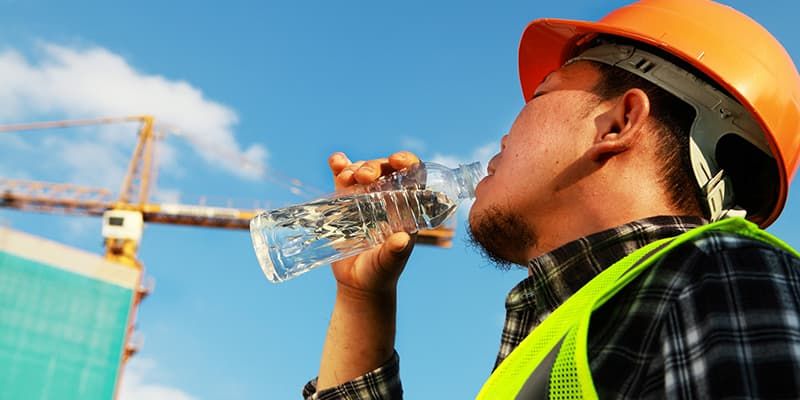 Site operative wearing orange hard hat and yellow hi-vis vest drinking a bottle of water